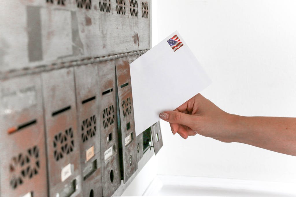 Close-up of a hand inserting a stamped envelope into a mailbox, symbolizing voting.